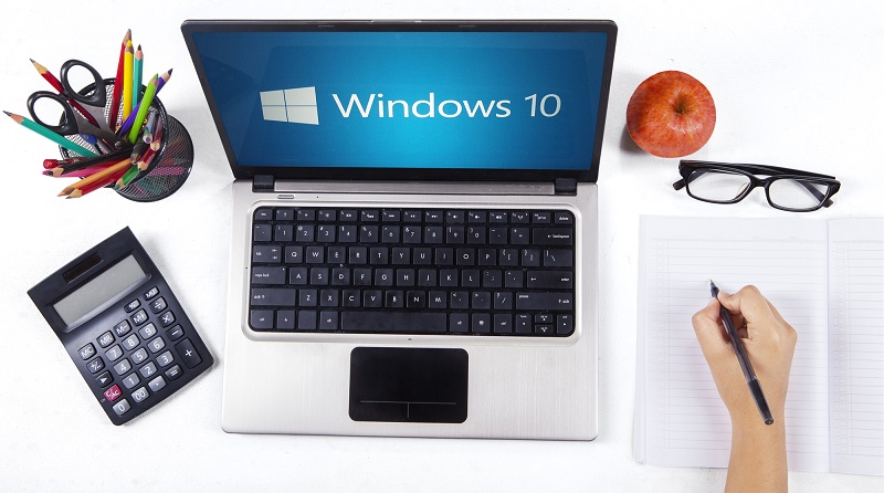 Closeup of a notebook computer with windows 10 logo and a student hand writing on the book